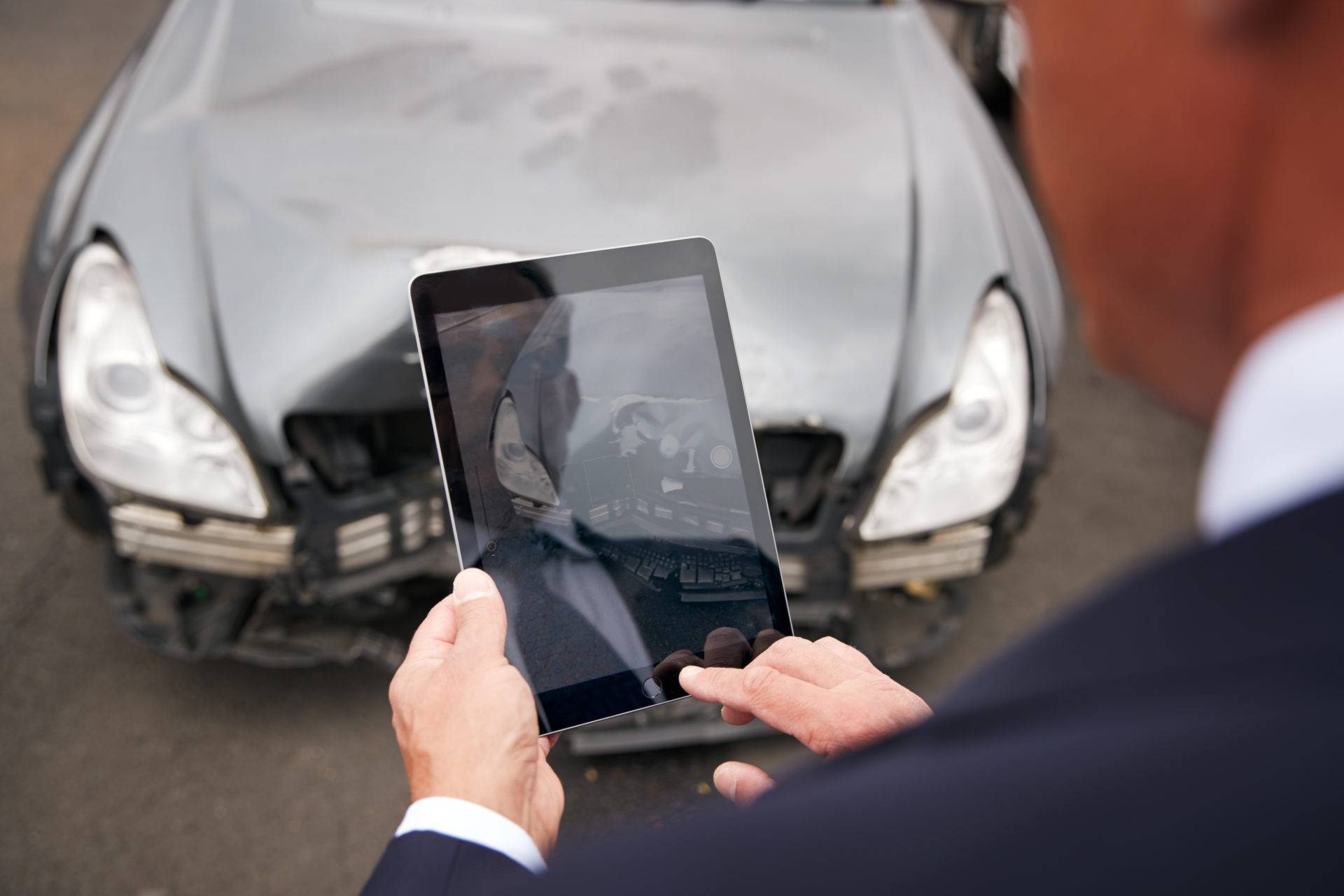 insurance loss adjuster taking picture with digital tablet of damage to car from motor accident